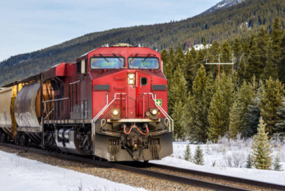 Cargo Train through the Canadian Rockies on a Sunny Winter Day. The Ground along the Track is Covered in Snow and a Thick Forest is in Background. Motion Blur.